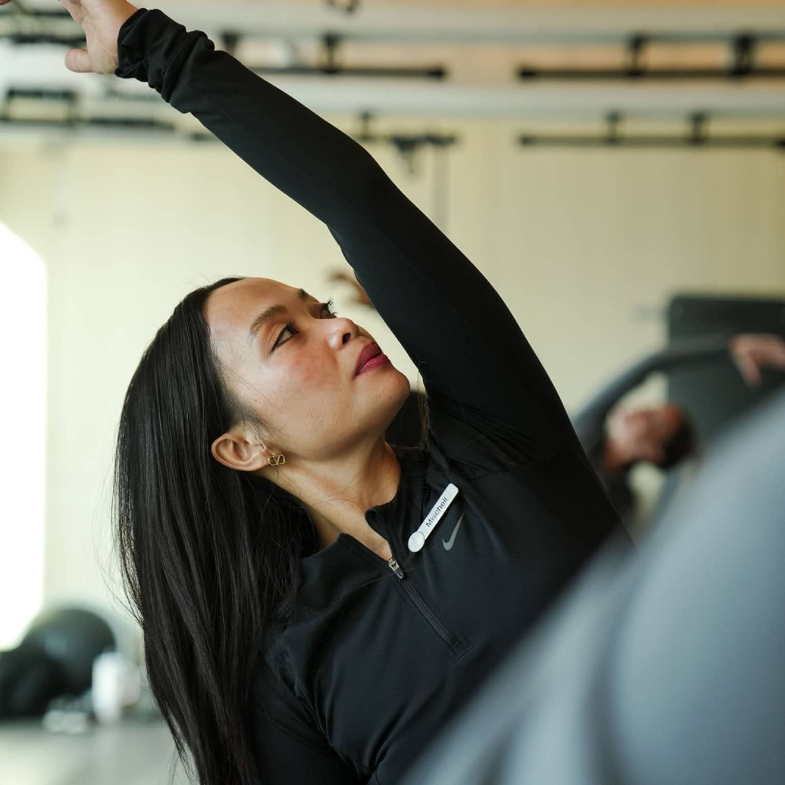 Person with long dark hair wearing black atheltic clothing stretches their arm over their head