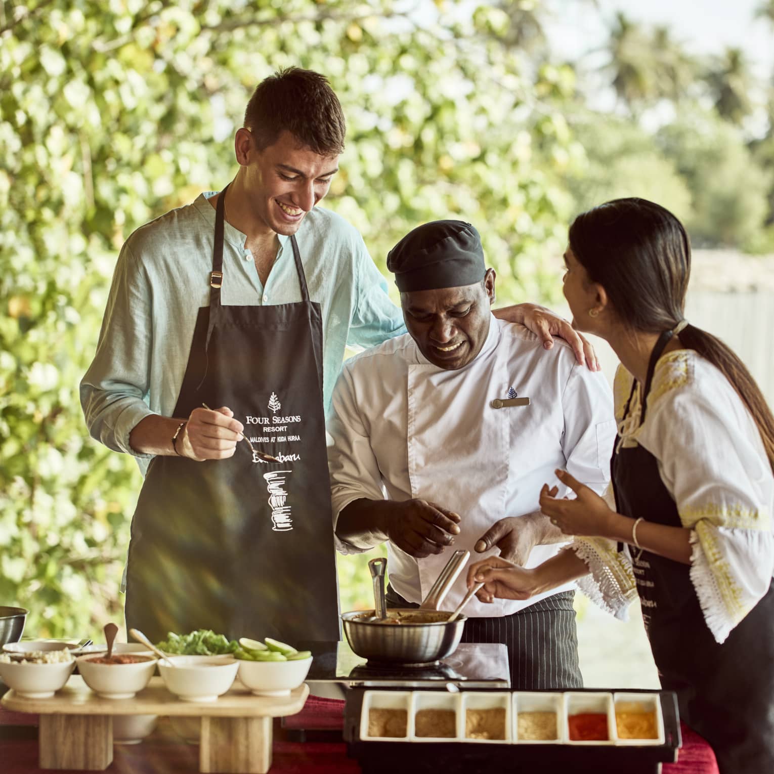 Chef teaches two guests how to make traditional Indian dish in outdoor kitchen