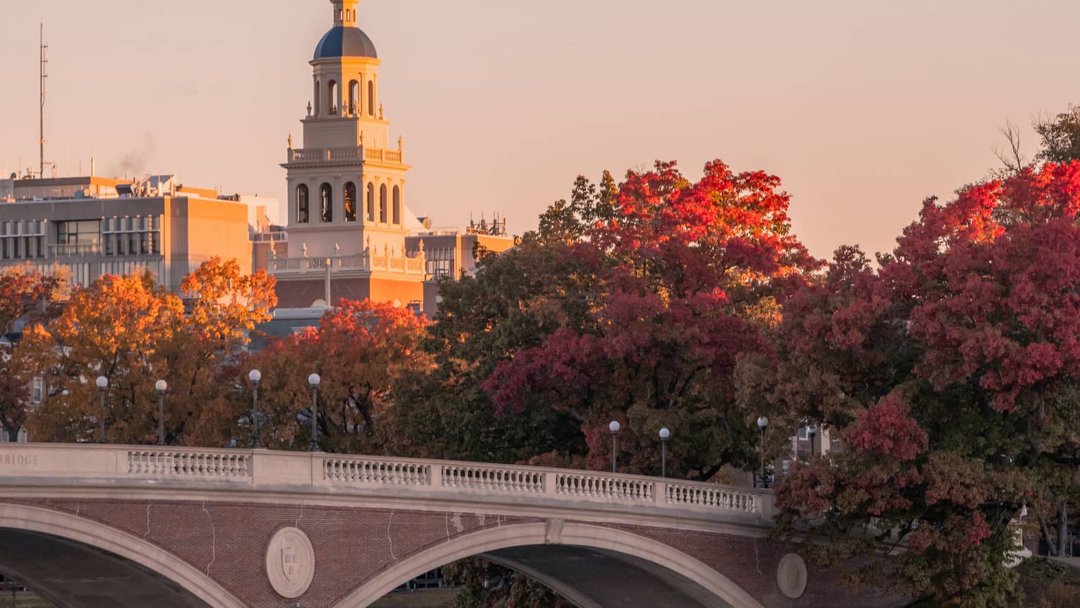A square bell tower overlooks radiant red and orange maple trees and a red-brick bridge lined with globed street lights.