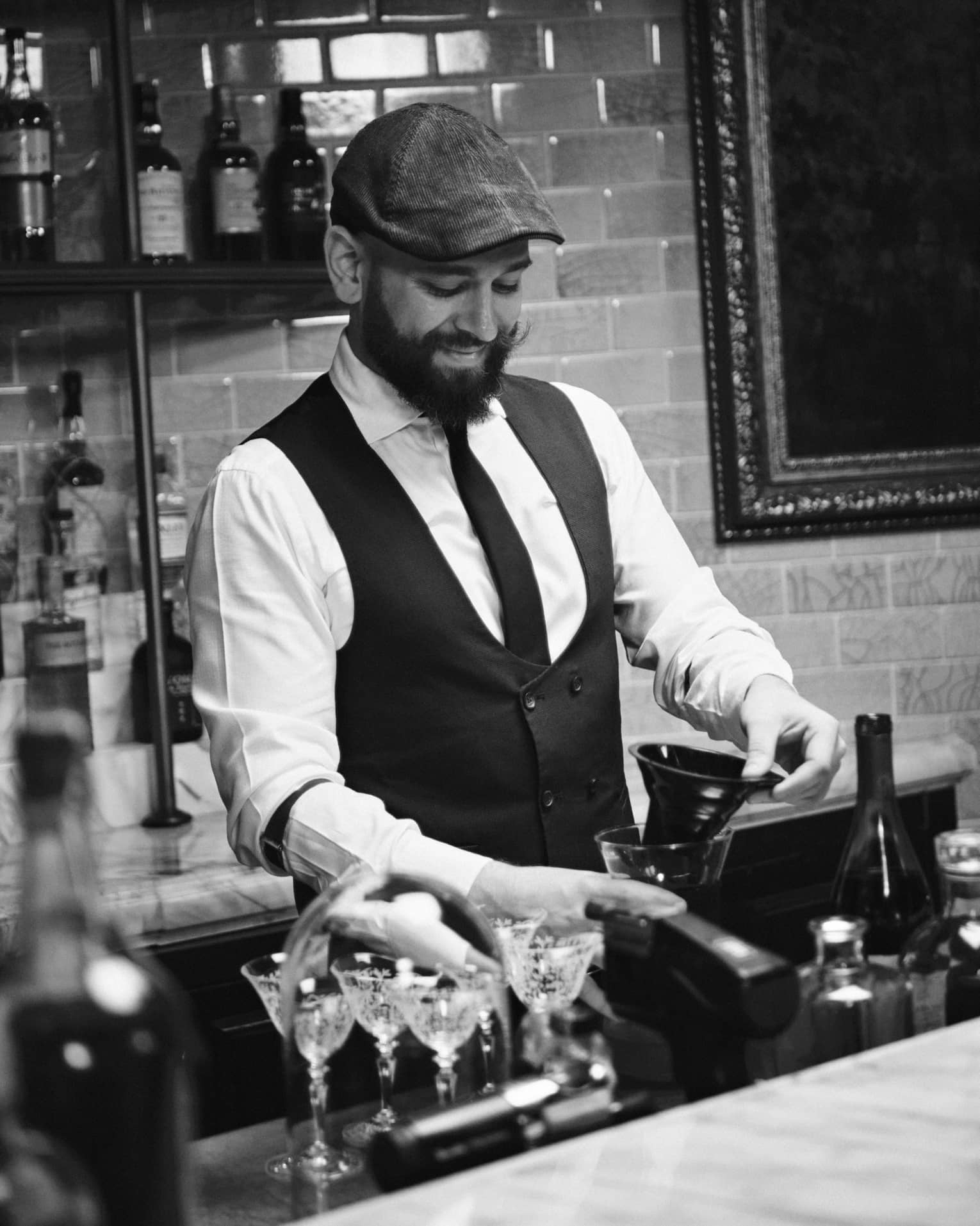 A bartender wearing a tie and vest works behind a bar