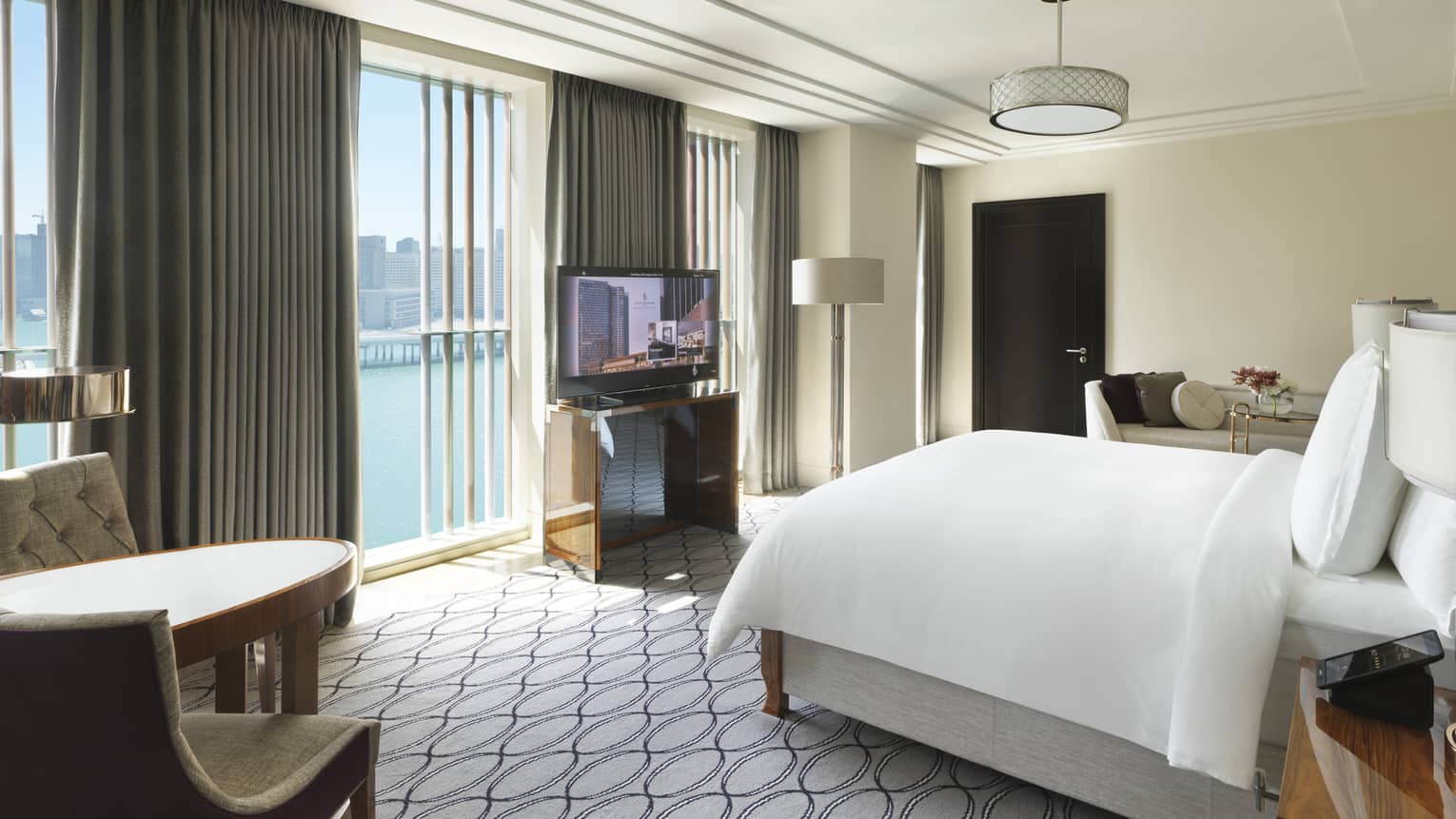 Hotel room with king bed, table with two chairs, TV and wall of windows