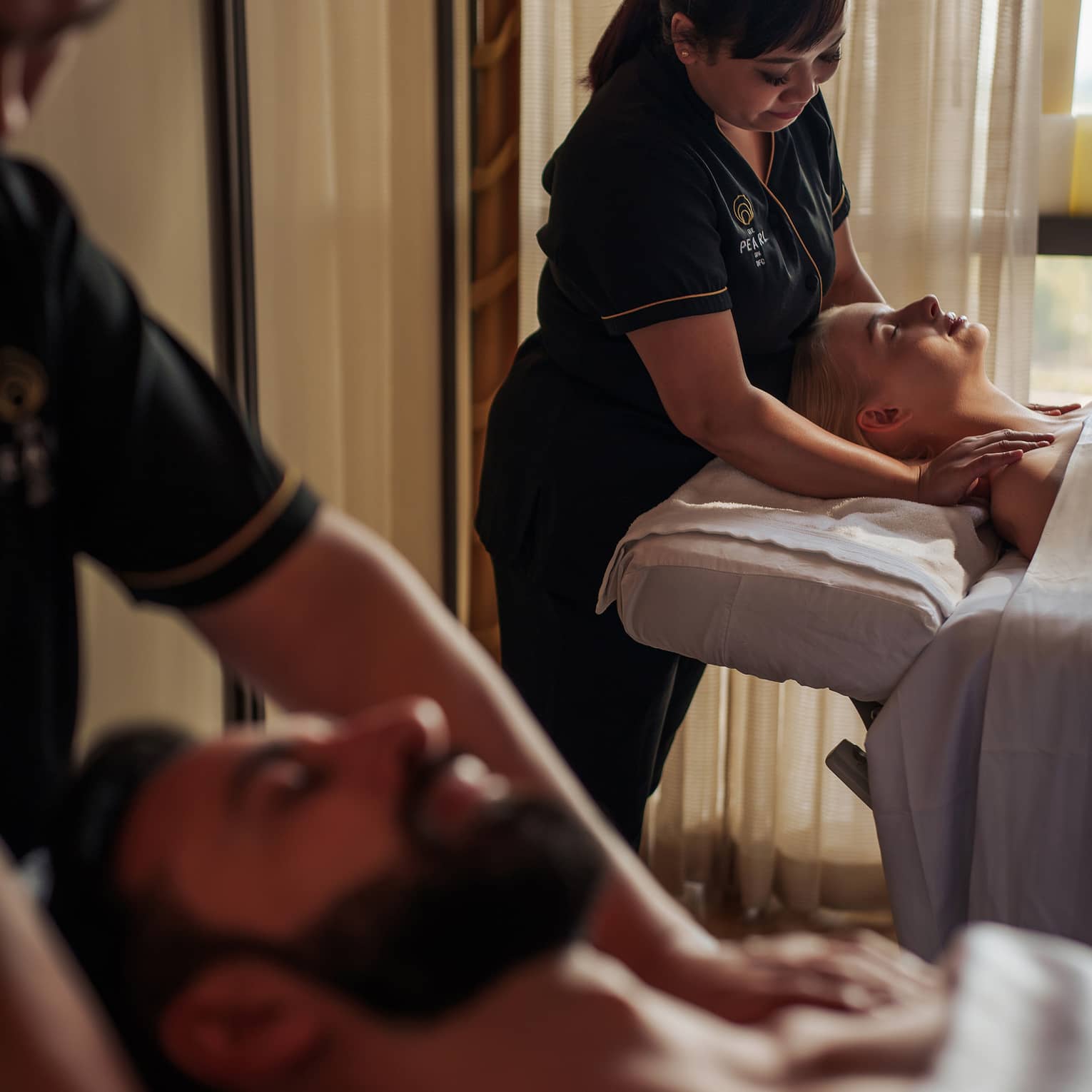 A two people receive a couple's massage in a serene spa treatment room.