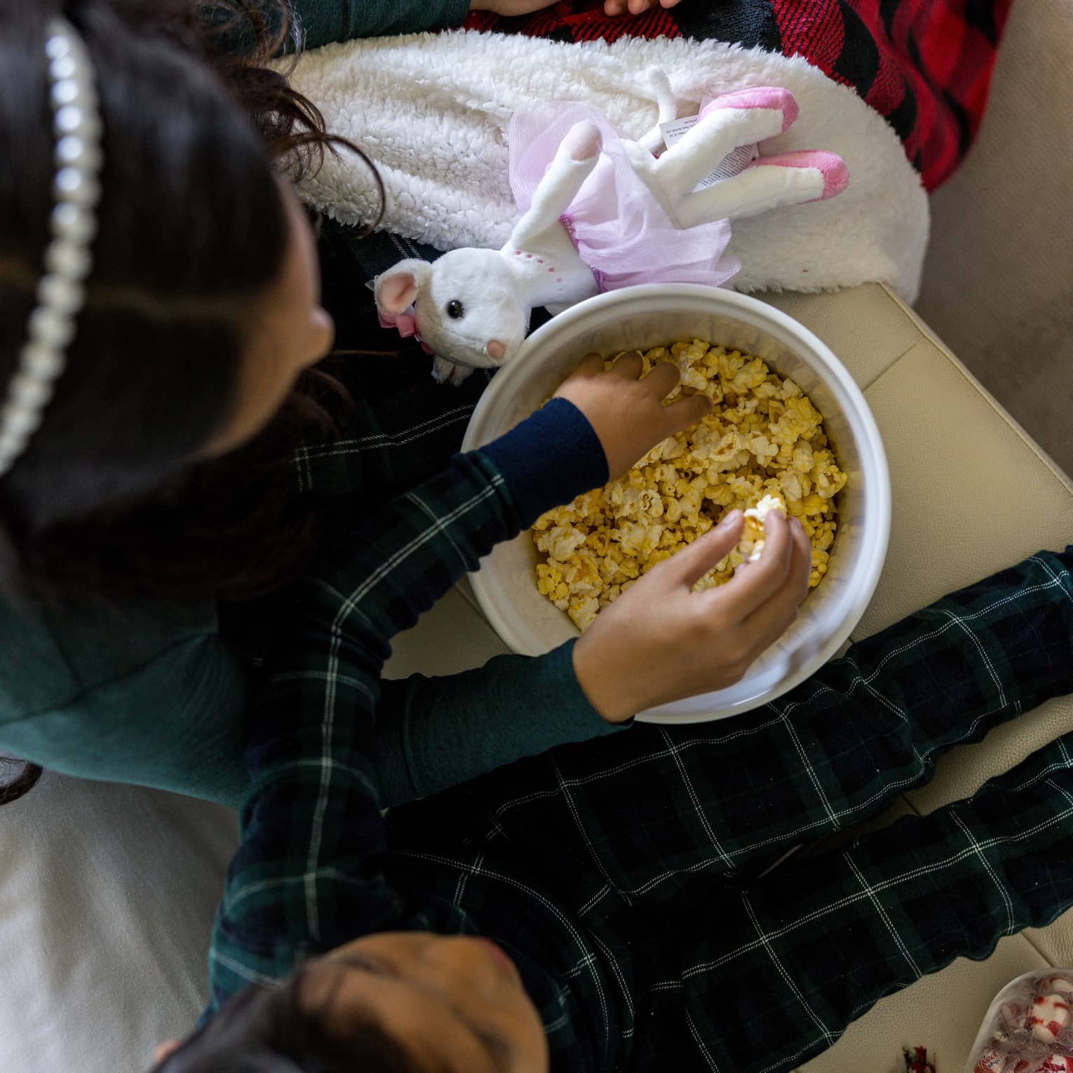 Two children wearing green pajamas sit on a couch sharing a bowl of popcorn