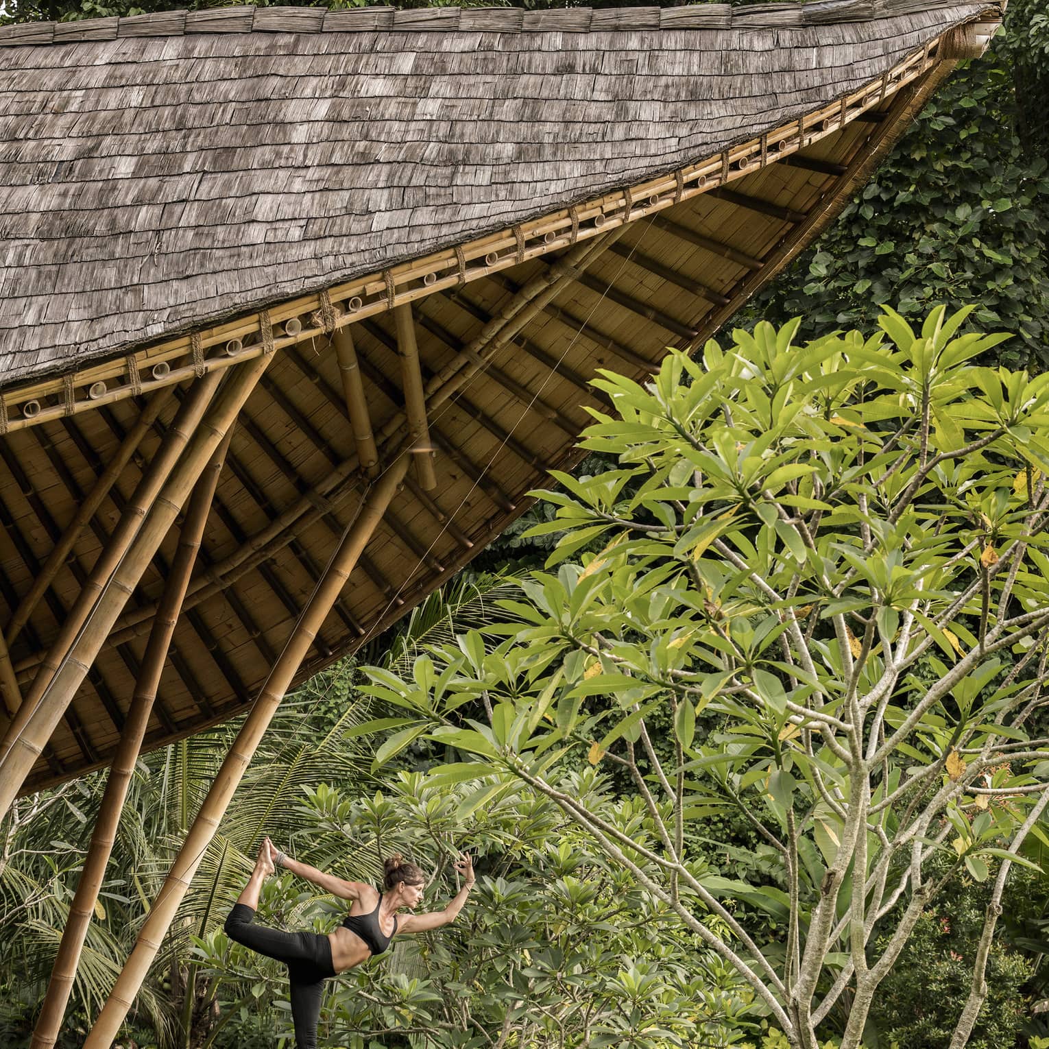A guest with her arms and leg outstretched, doing yoga in an outdoor pavilion