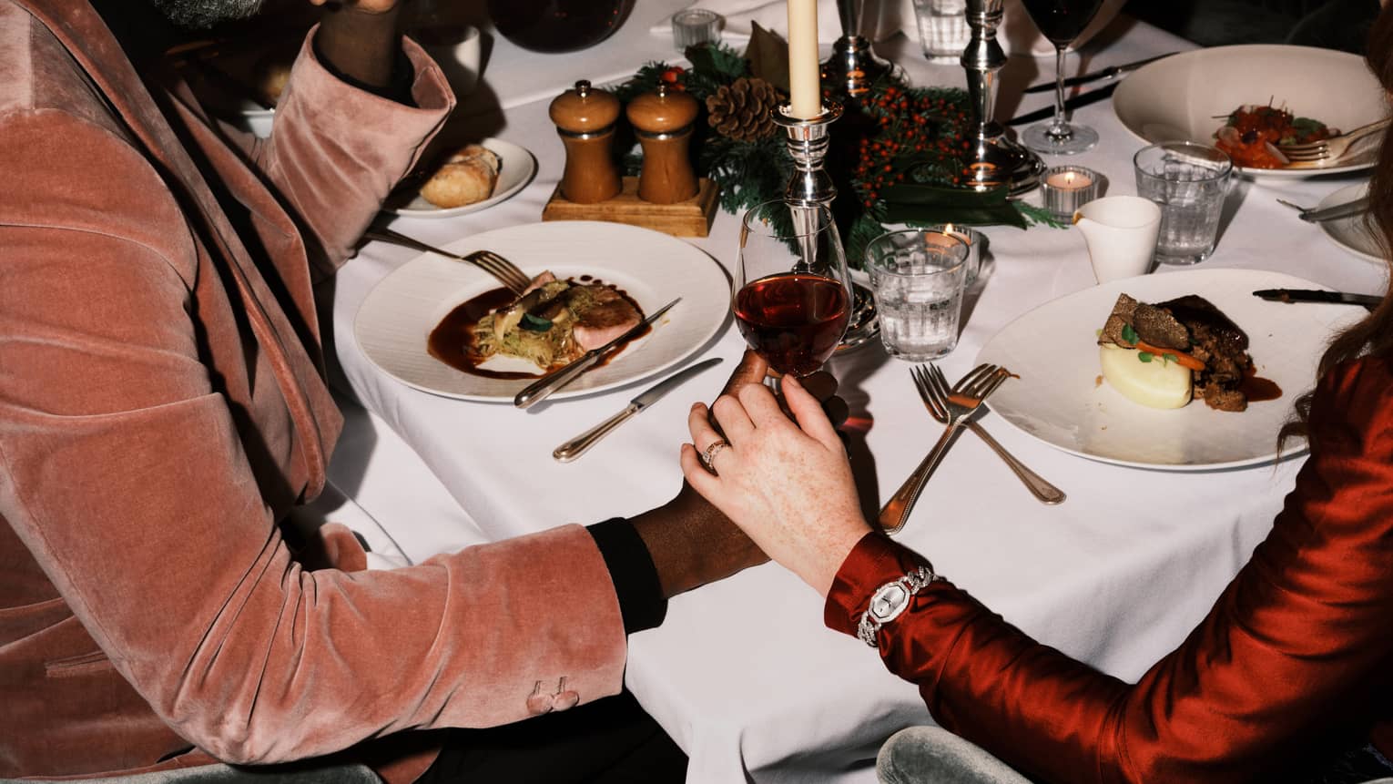 Two guests sitting at a dining table holding hands and a glass of wine.