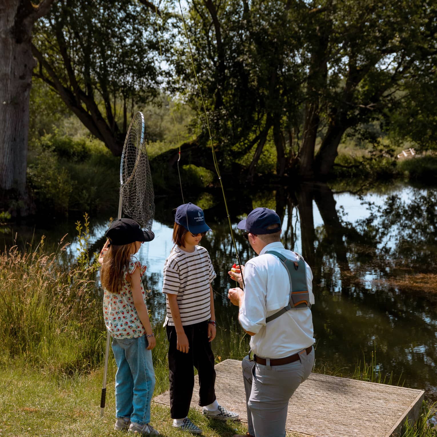 Fishing instructor holding fishing rod and kneeling in front of two children with one holding a net