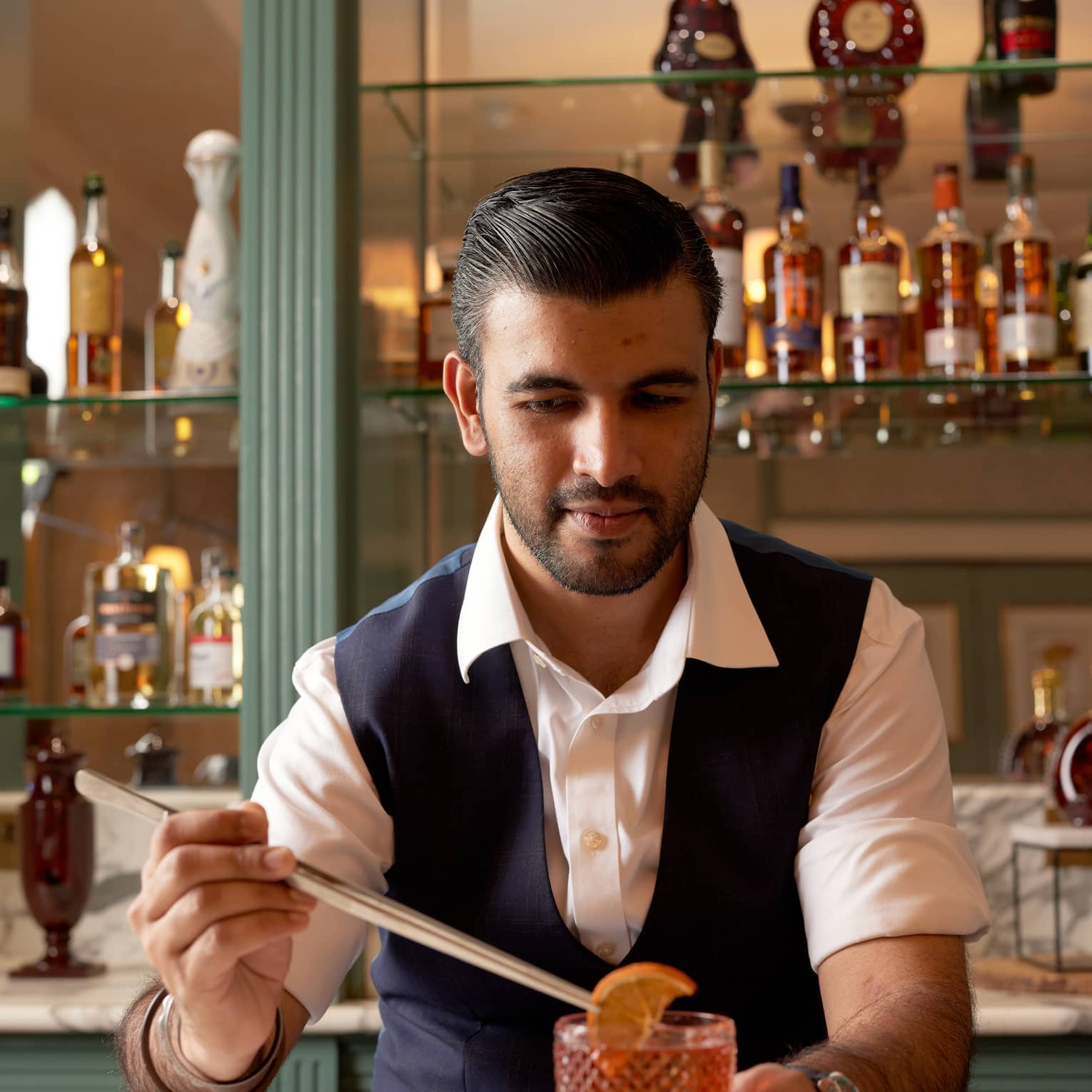 Bartender behind bar garnishing a negroni with an orange slice using long tongs