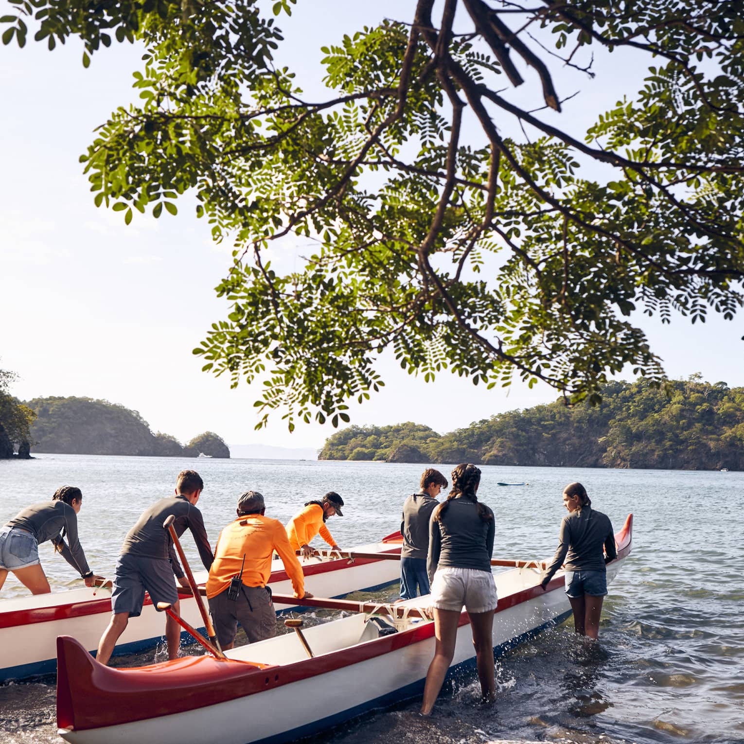 A group of people pushing canoes out onto water.
