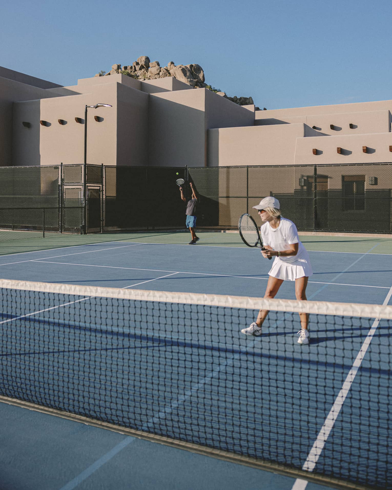 Two guests playing tennis on an outdoor tennis court.
