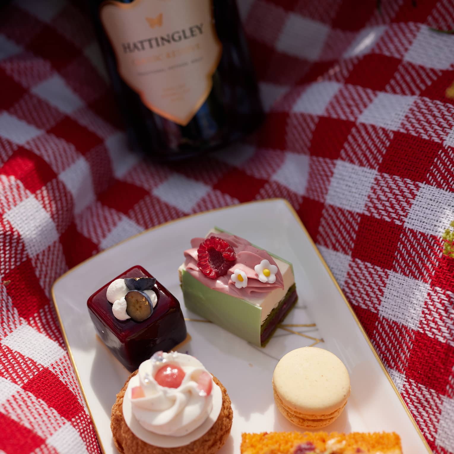 Desserts on a plate placed on a picnic blanket and a bottle of wine beside it