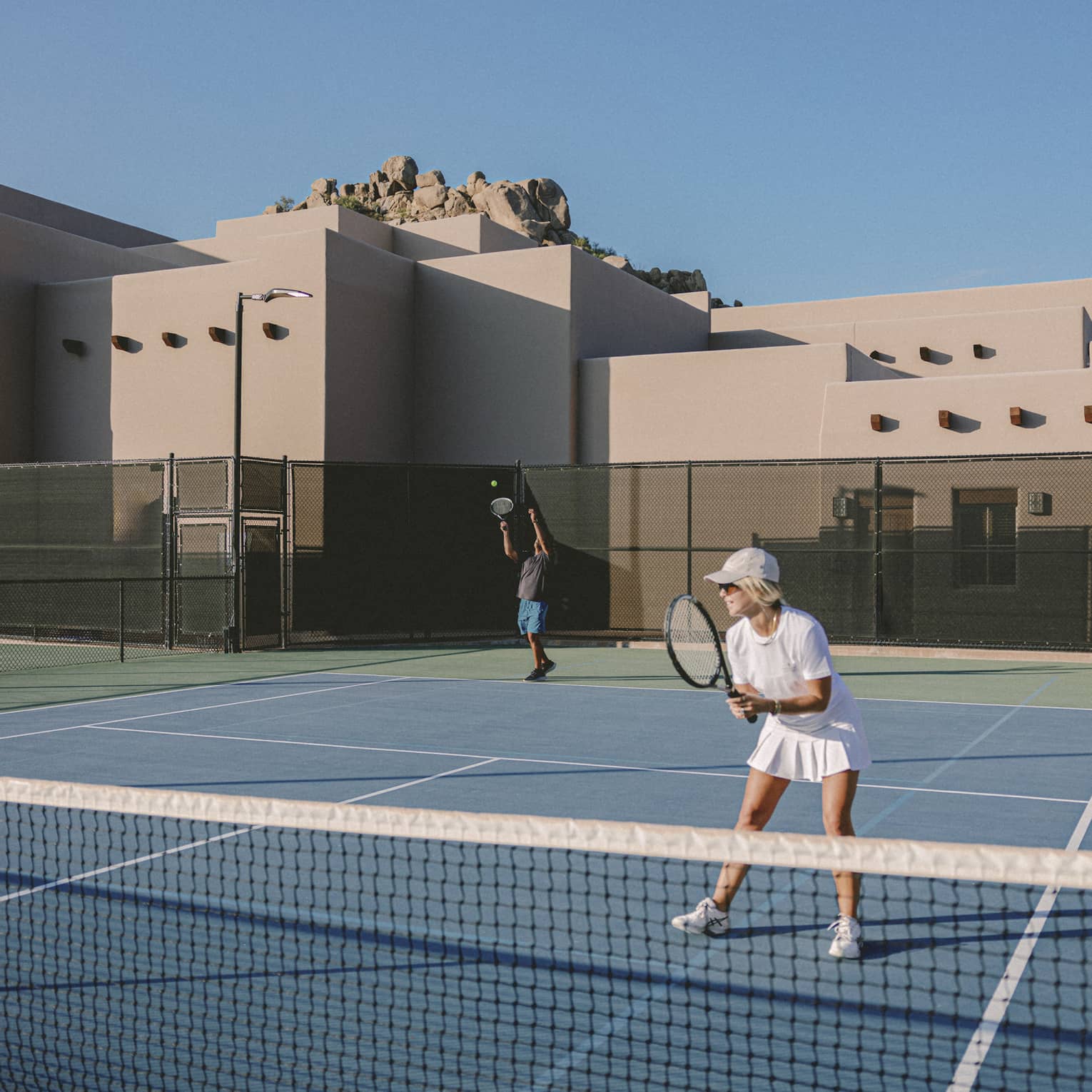 Two guests playing tennis on an outdoor tennis court.