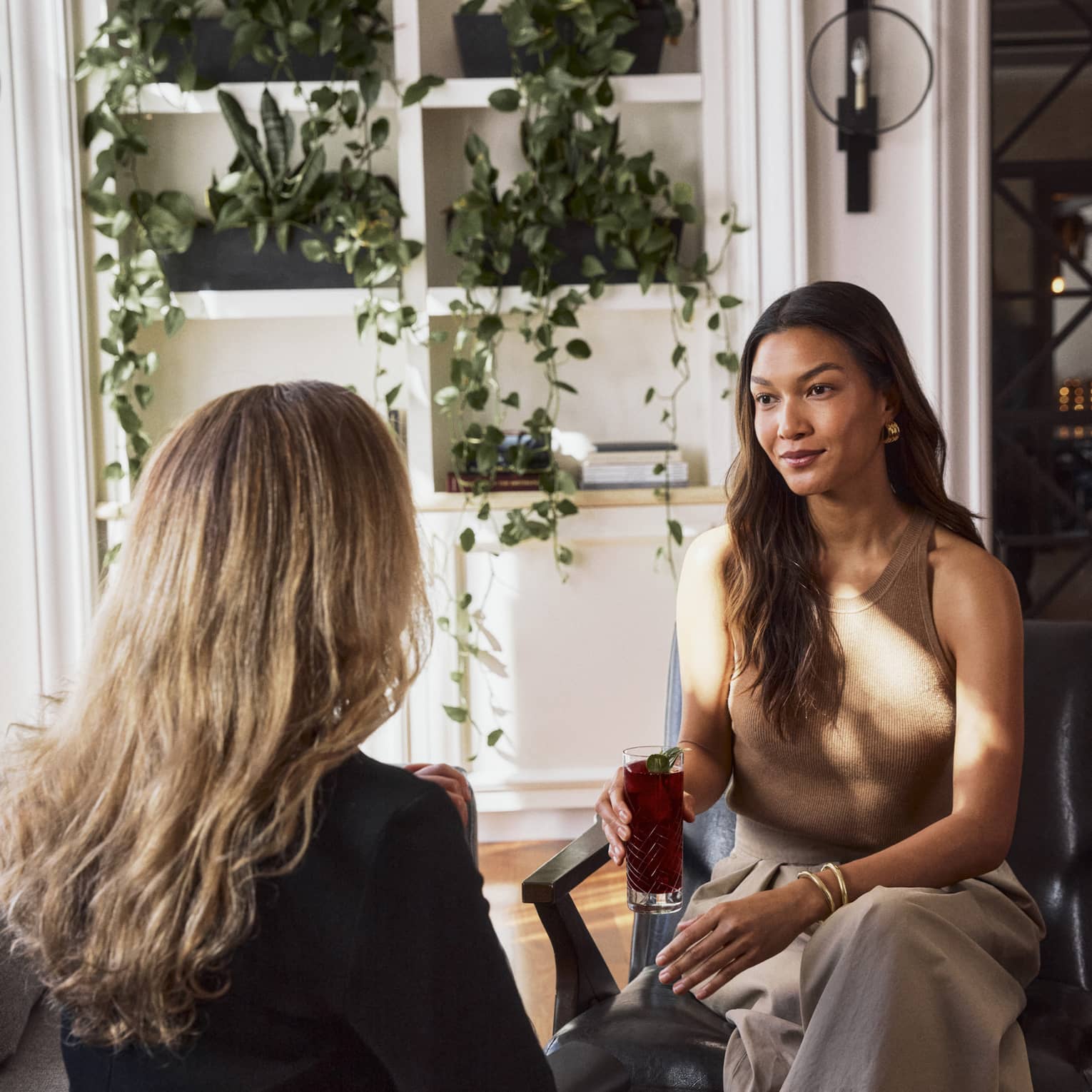 Two guests sitting in chairs facing one another, the wall behind them has four plants.