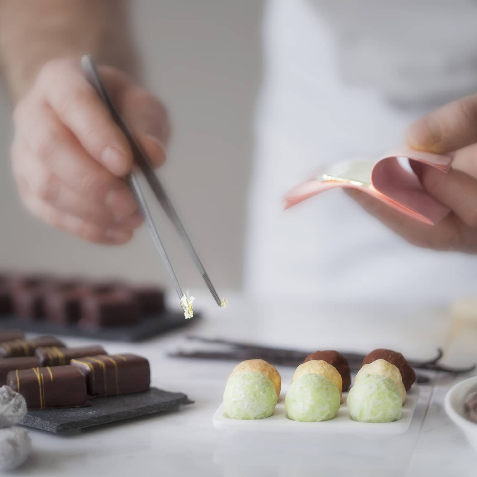 A close up of a male chef's hands using tongs to place various chocolates on parchment paper