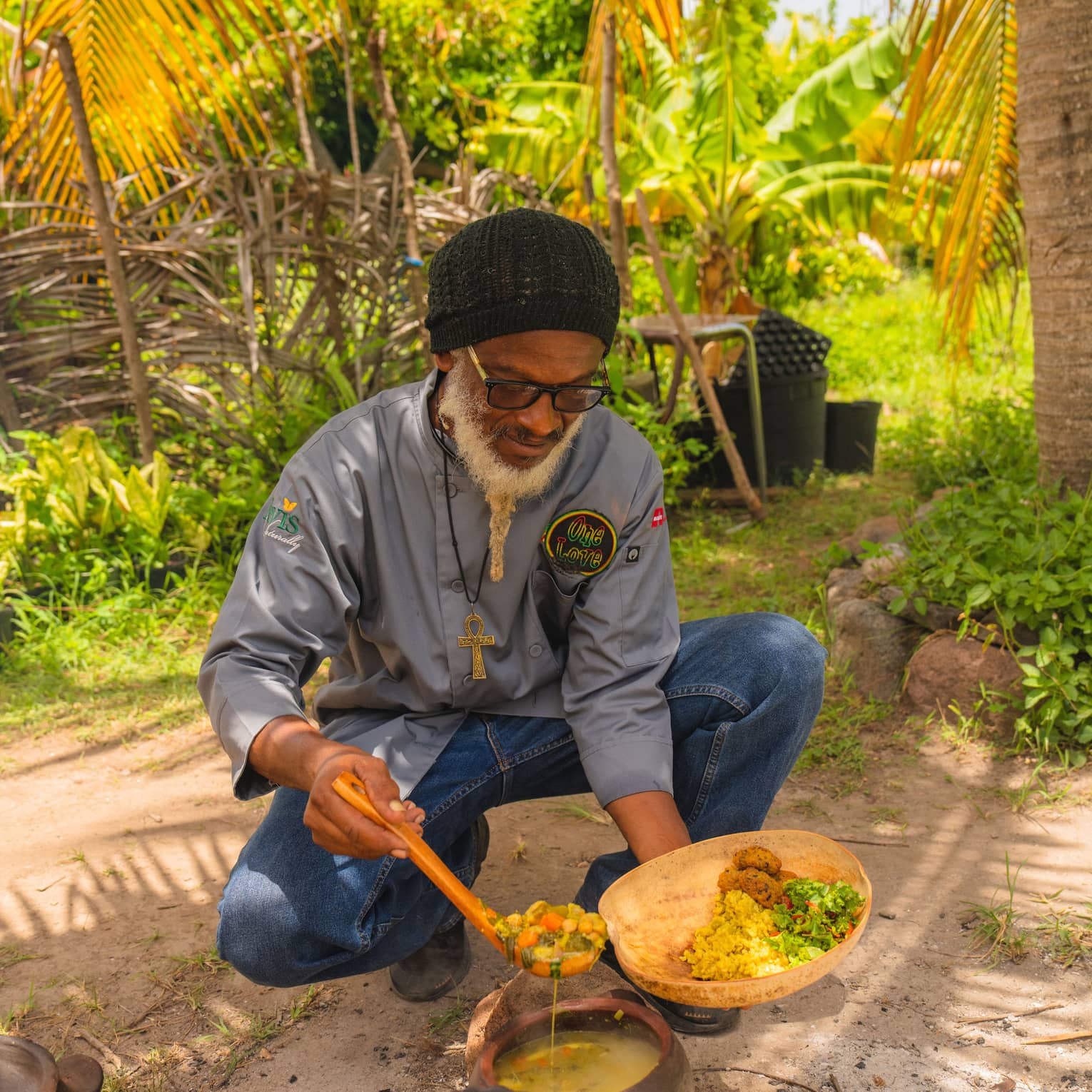 A man cooking outside amongst palm trees.