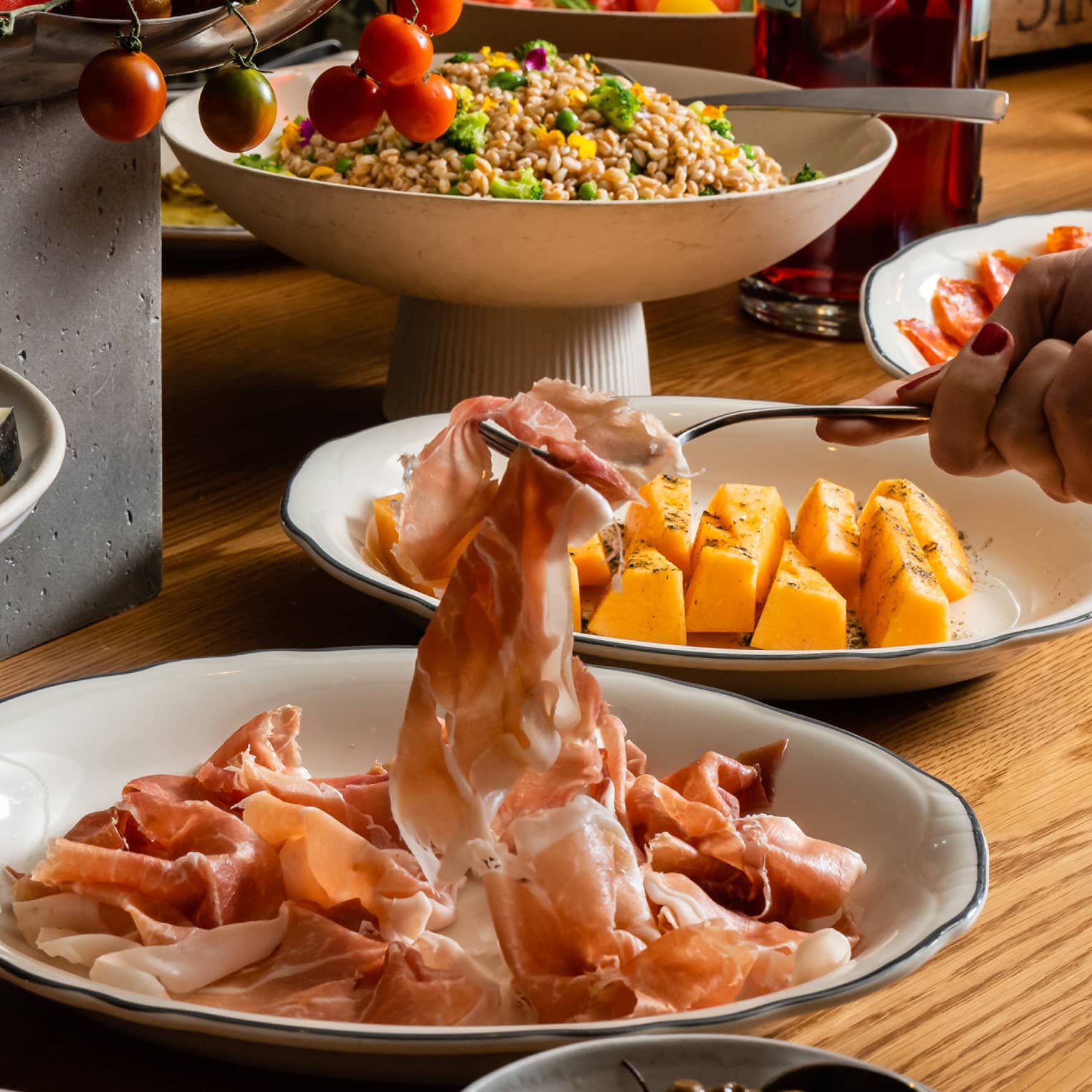 An aperitivo table laden with beautifully plated meats, olives and salads, a fork lifting a slice of prosciutto.