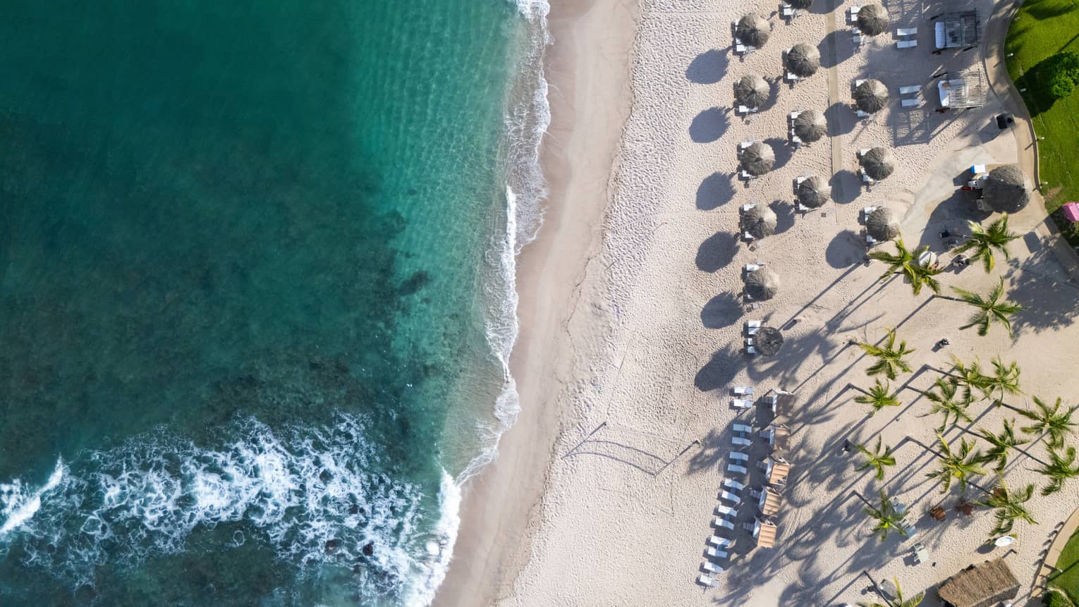 Aerial view of white-sand beach with umbrellas and sun loungers at tropical beach resort