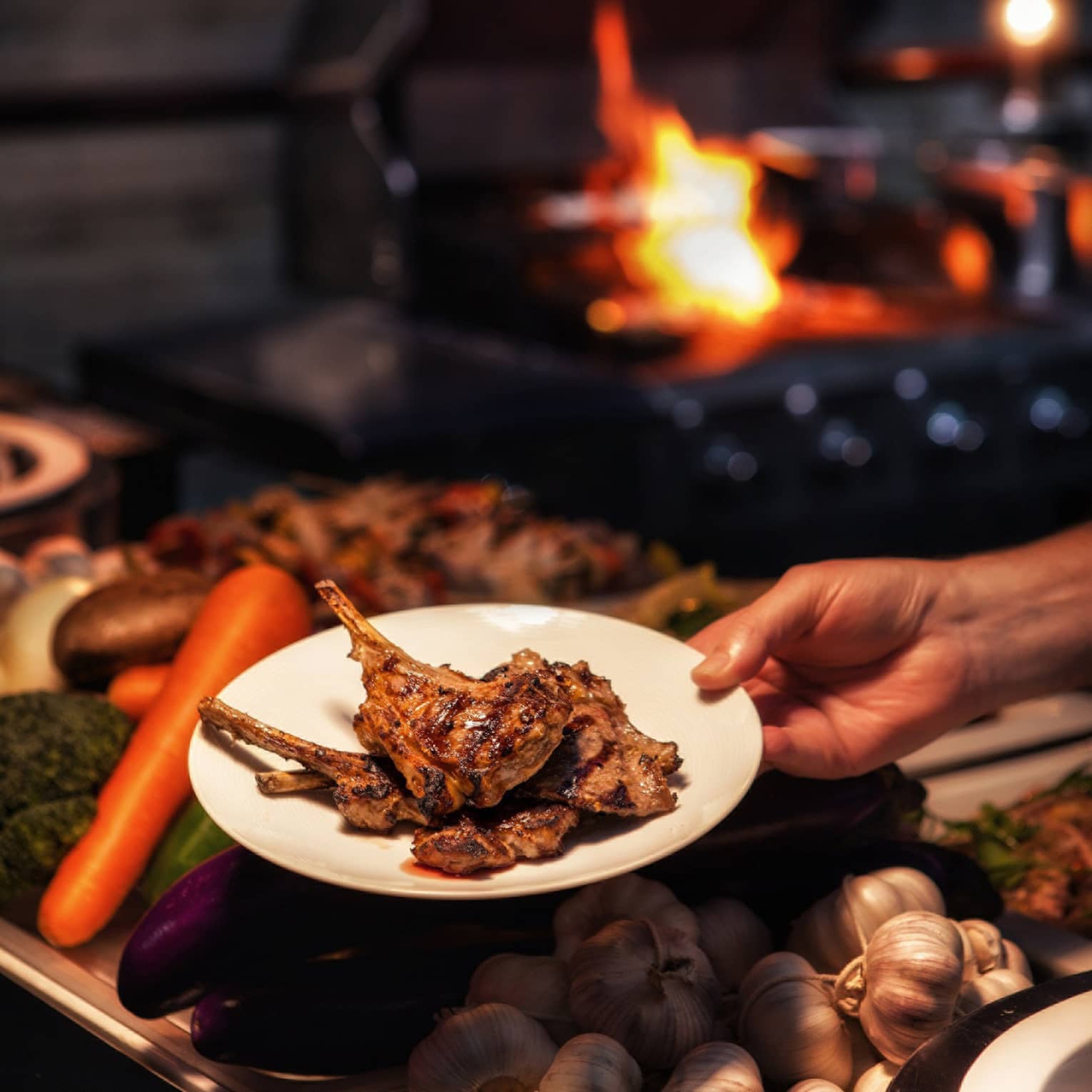 Hand holding barbecued chops on plate over fresh vegetables
