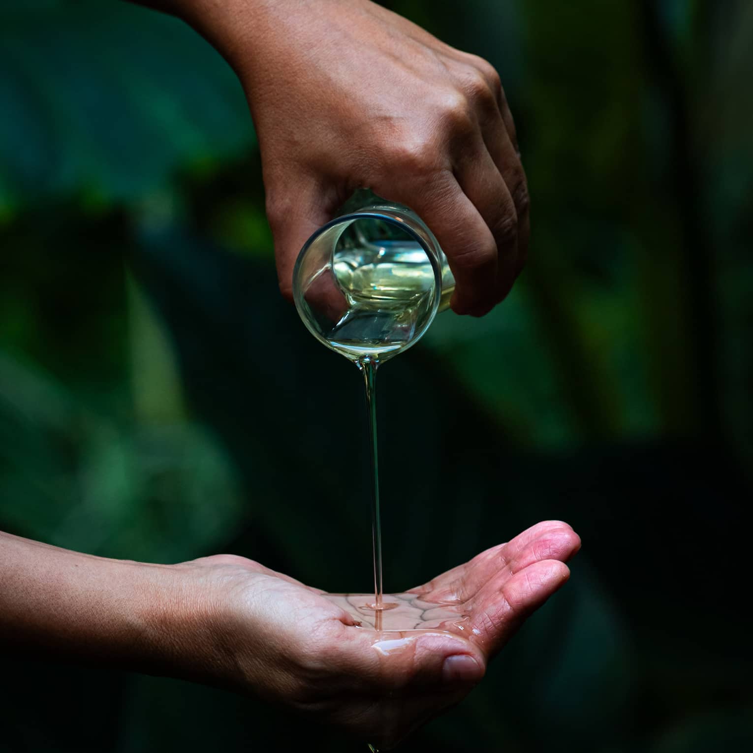 A person pours oil into cupped hand in garden setting