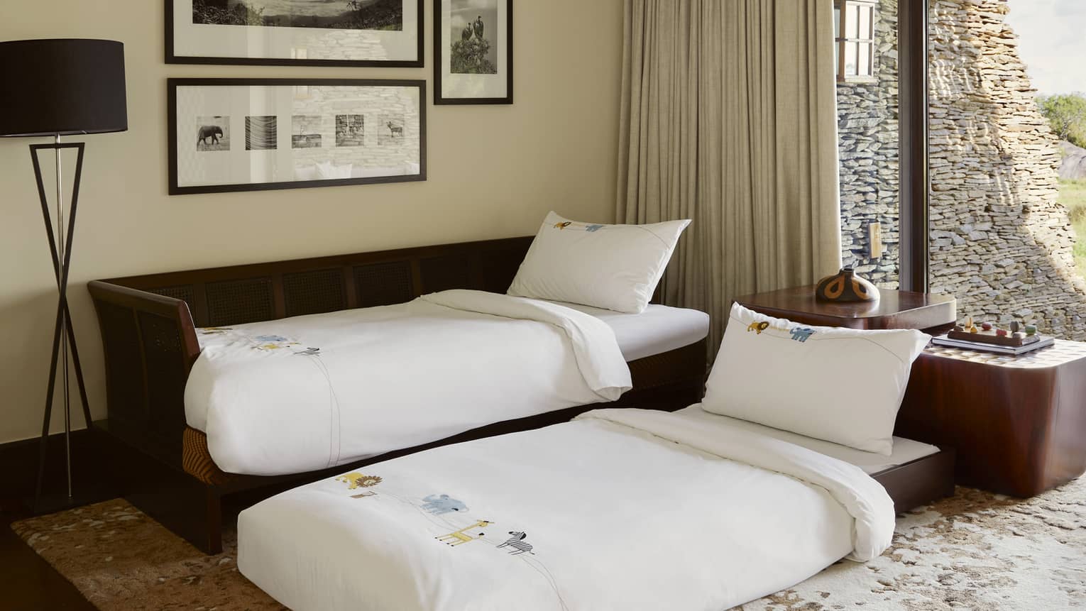 Brown twin trundle bed, against beige wall with black-and-white photos, with bottom bed extended