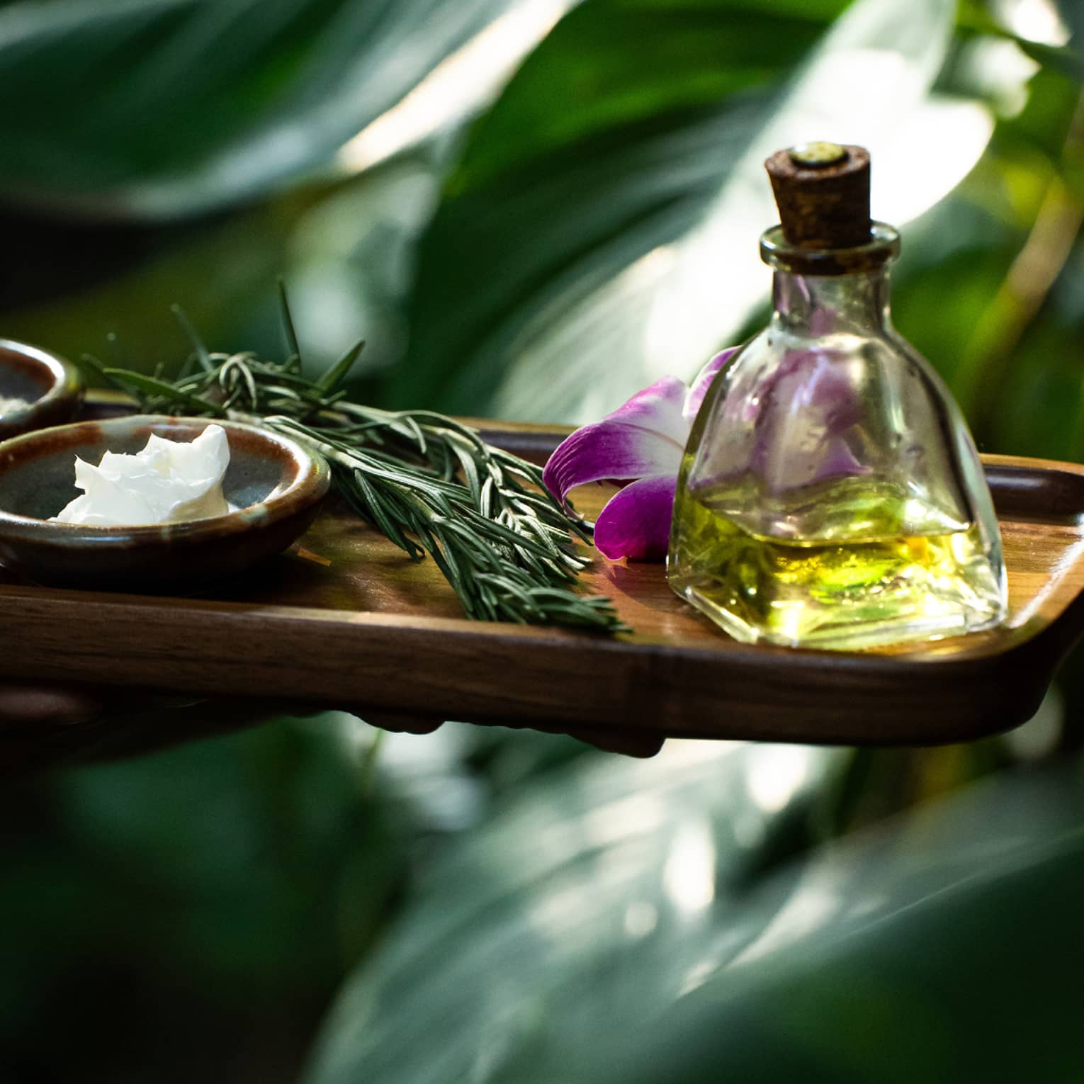 Spa oil, lotion and herbs on wooden tray in garden setting