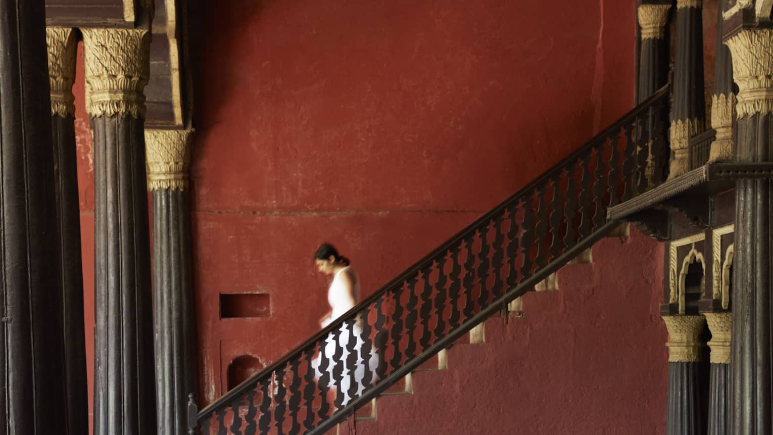 Side view of a guest descending a stone staircase, in a room supported by pillars with intricate gilded embellishments.