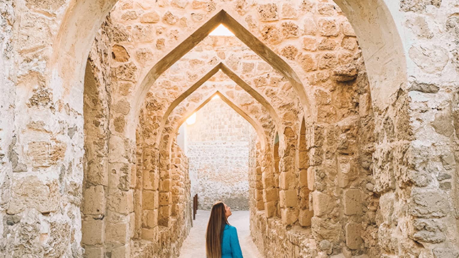 A woman stands underneath a stone pathway.