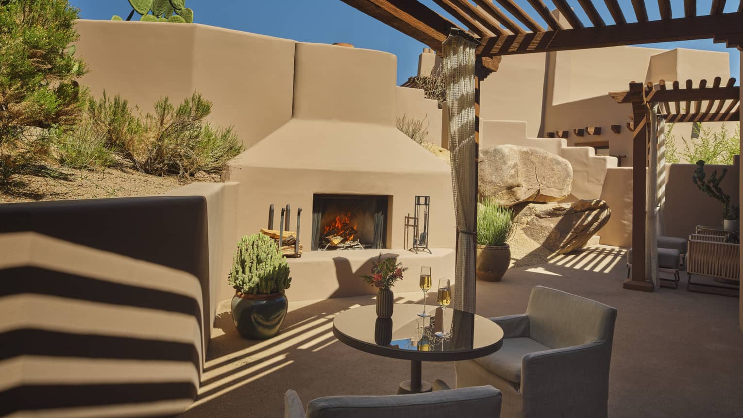 Private terrace of Southwestern resort suite, featuring a table with two chairs and an outdoor fireplace