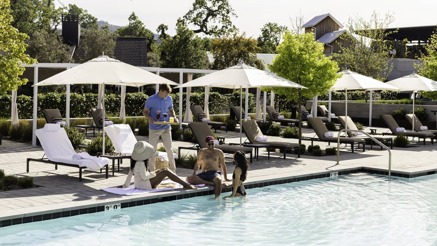 A person bringing a tray of beverages to three guests near the pool