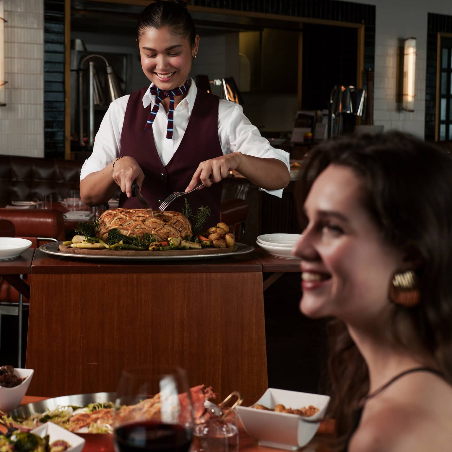 Served slices beef Wellington tableside as a patron smiles holding a glass of red wine