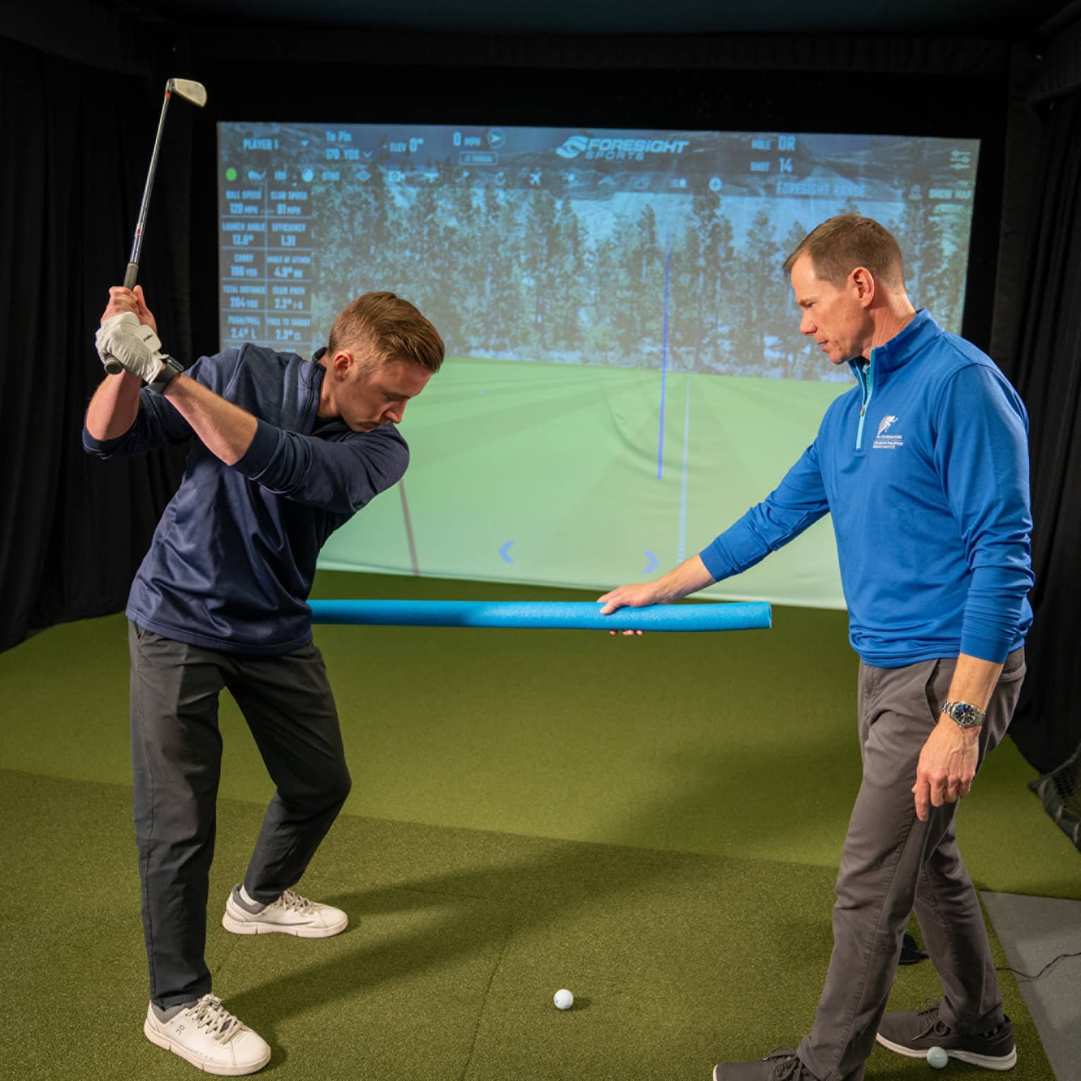 Two guests at a golf simulator, one guest swinging a golf club