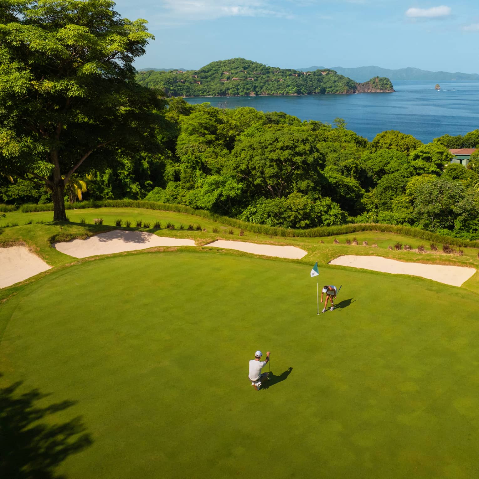 Aerial view of two golfers on a green with the ocean in the background