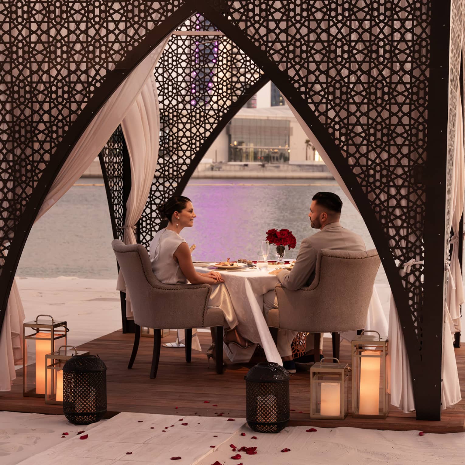 A couple dines in a beach cabana adorned with Arabian-style arches, candle lanters and rose petals along the walkway leading to the cabana