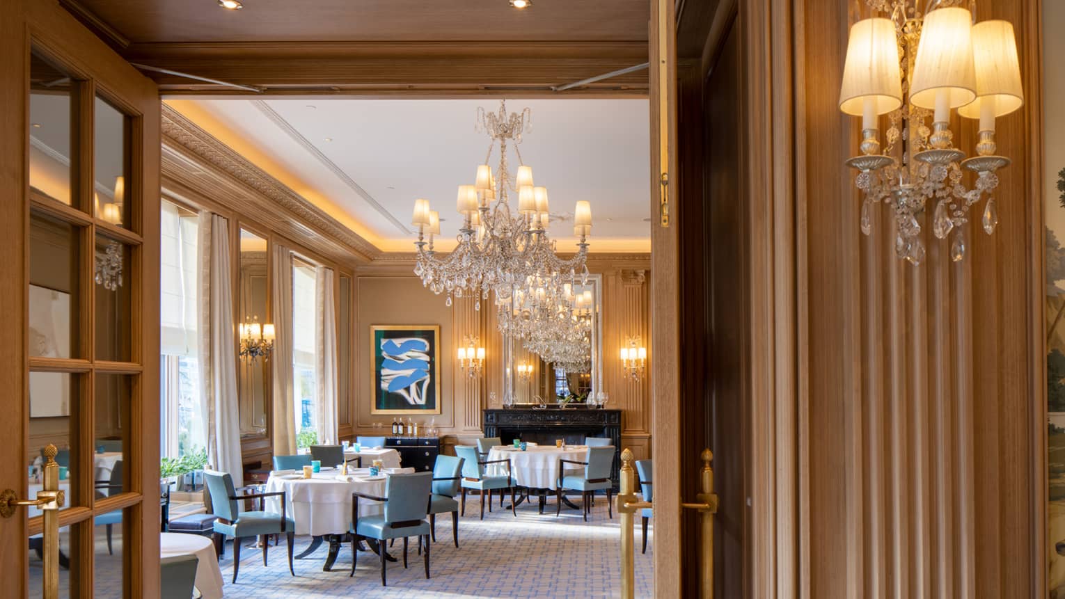 Dining area with blue chairs and round tables, crystal chandeliers and contemporary art