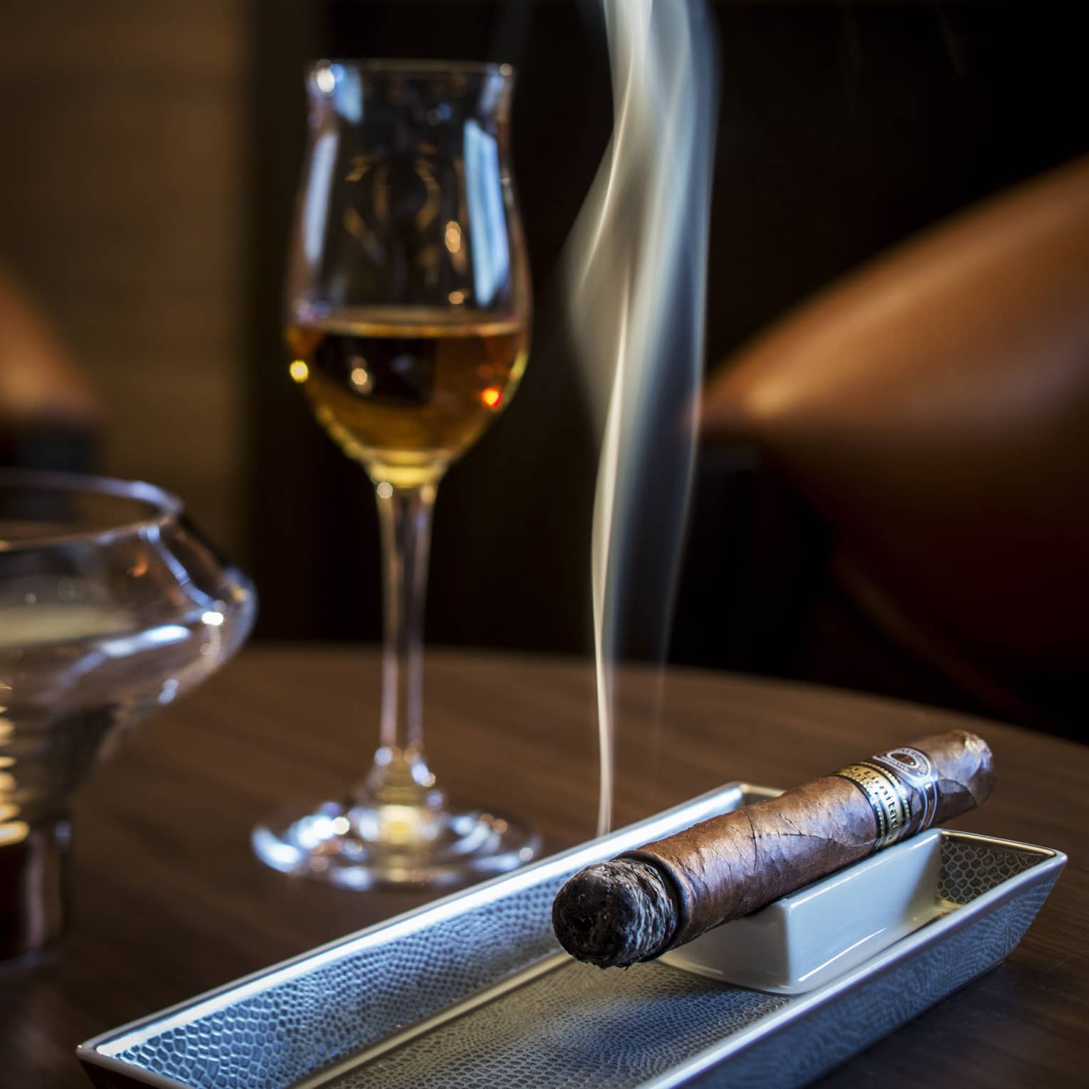 Smoking cigar on tray under glass with liquor