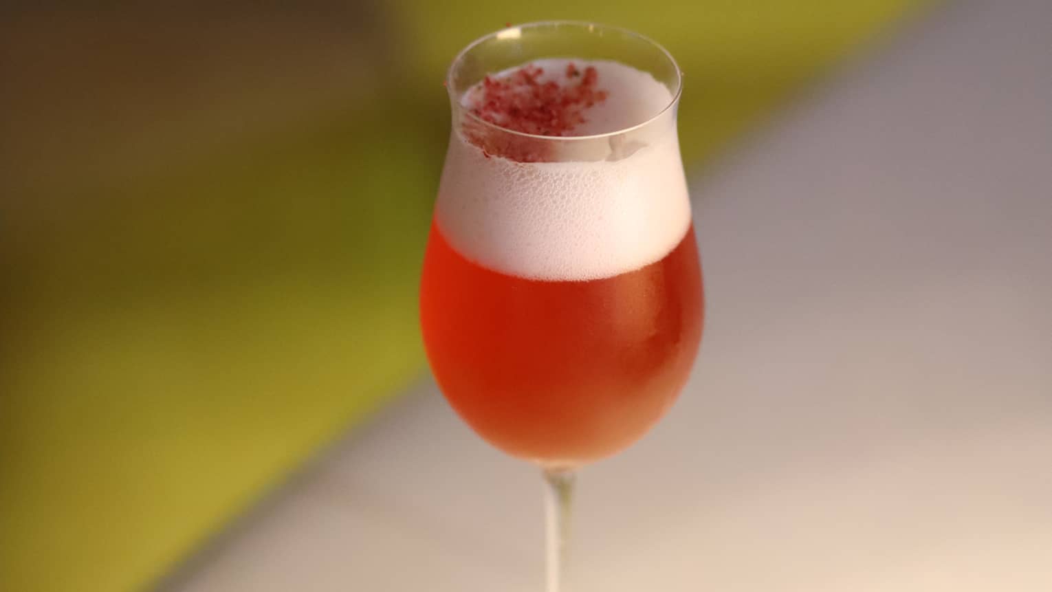 A strawberry drink with foam on top in a tall glass on a table