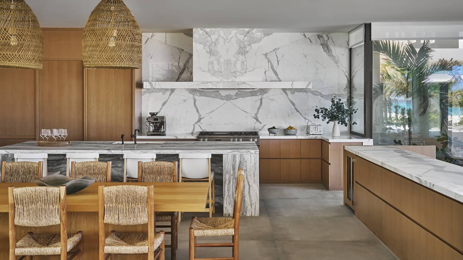 Modern kitchen of a luxury villa at Four Seasons Resort and Residences Los Cabos, with modern walls and countertops, rattan dining chairs and hanging lights