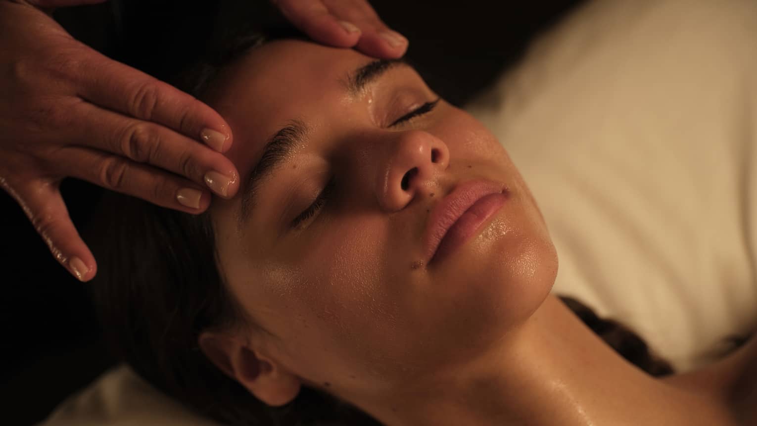 Guest lies with eyes closed as hands massage her face