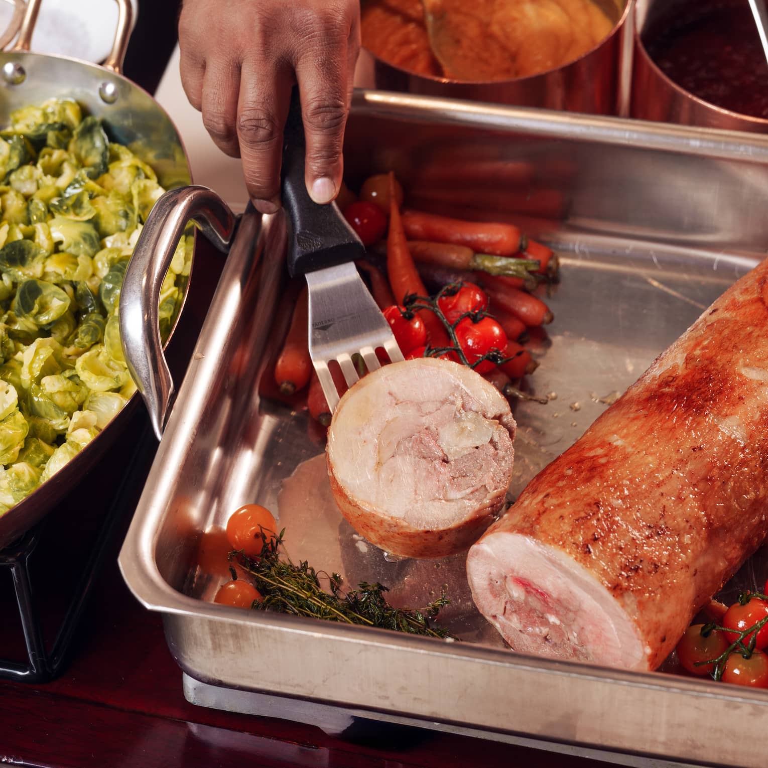 A chef's hands lift a slice of turkey out of a silver pan