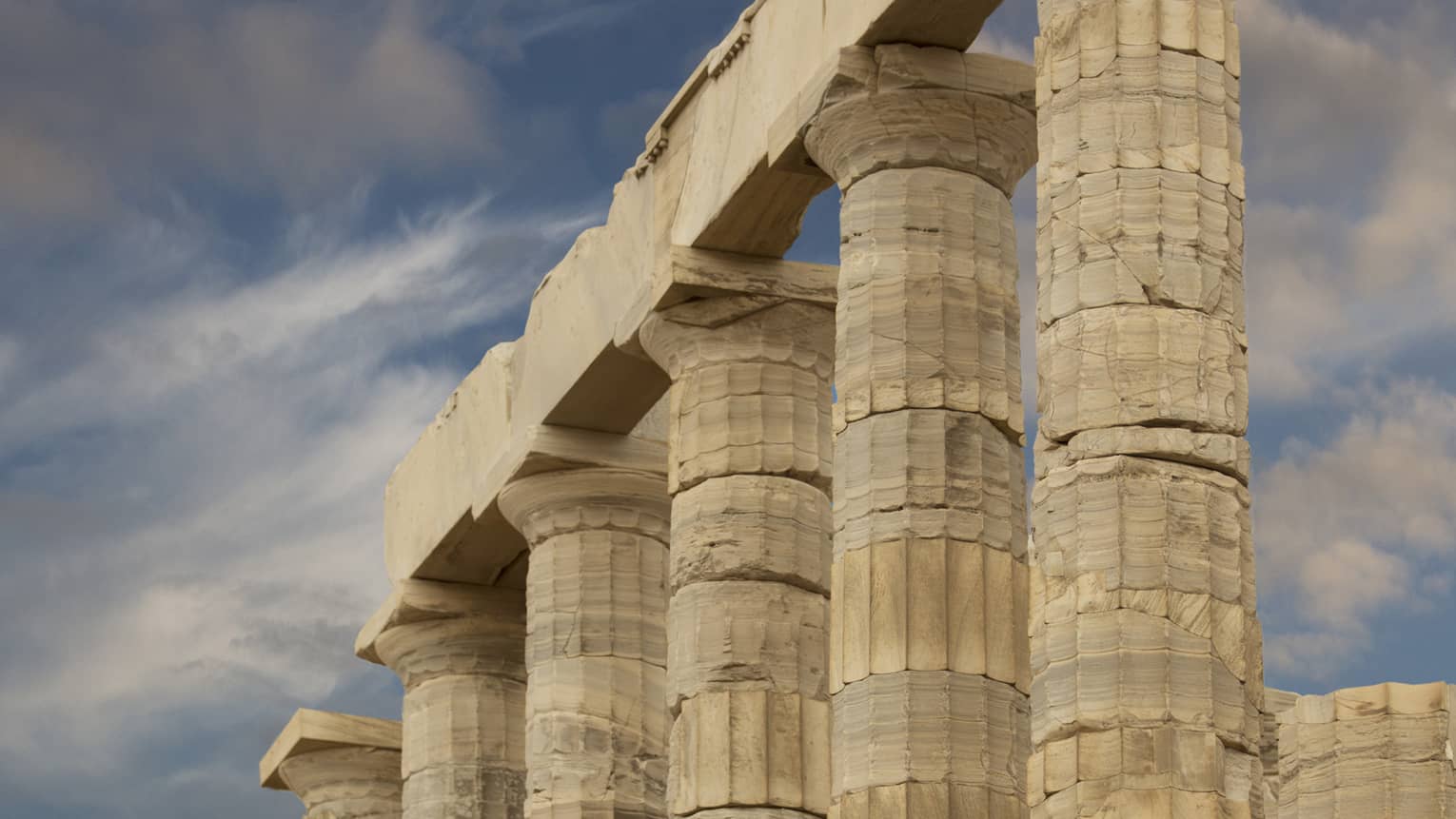 From the bottom of stairs, view of ancient towering Doric columns with vertical grooves atop a jagged brick foundation.