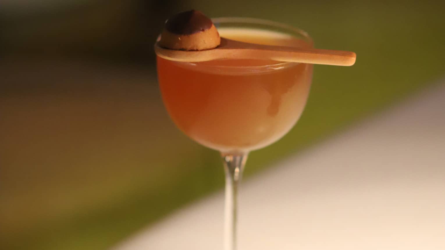 A wine glass on a coaster with a small spoon balanced on top of it