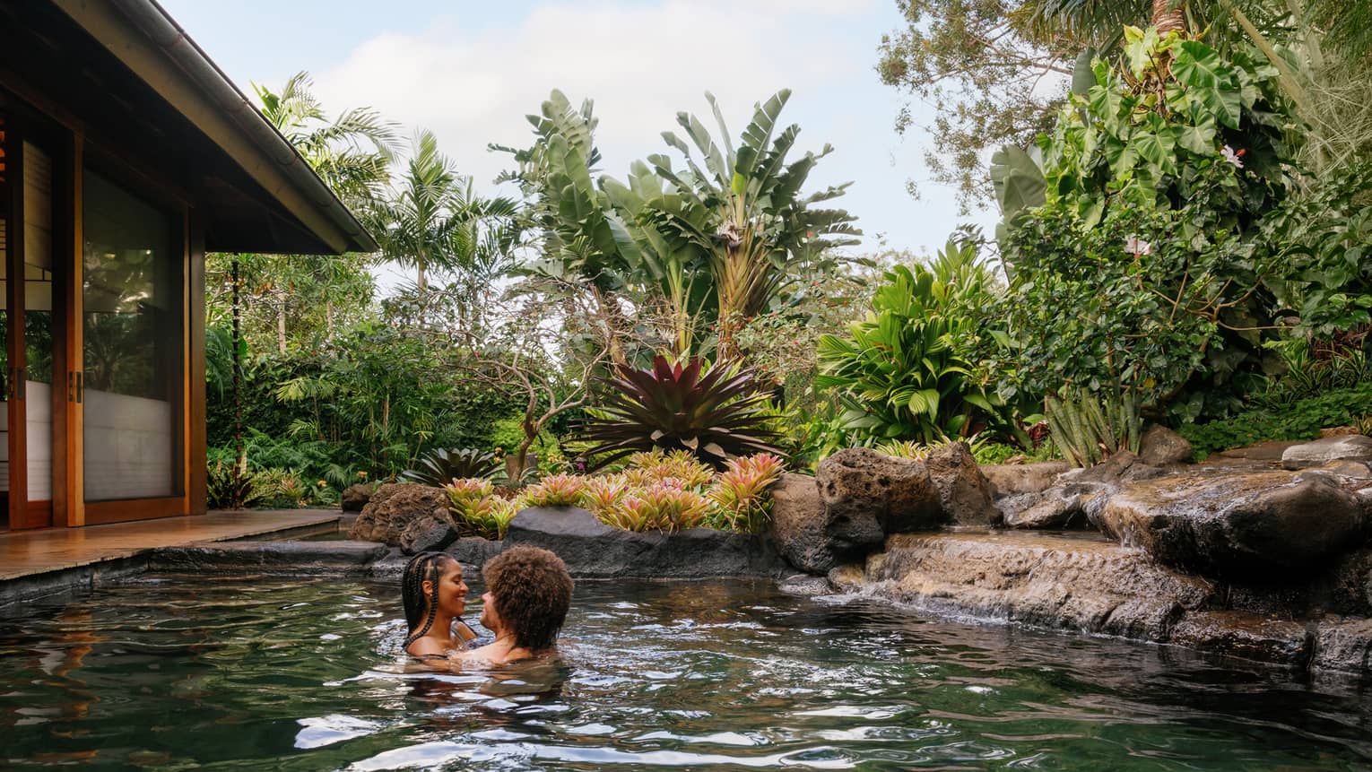 A man and woman embrace in a pond-like pool at a tropical resort