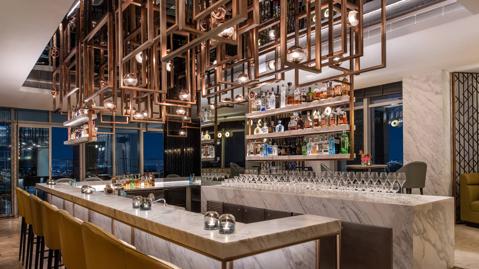Marbled bar area with mustard-coloured chairs, ornate metal sculpture above head and liquor bottle display