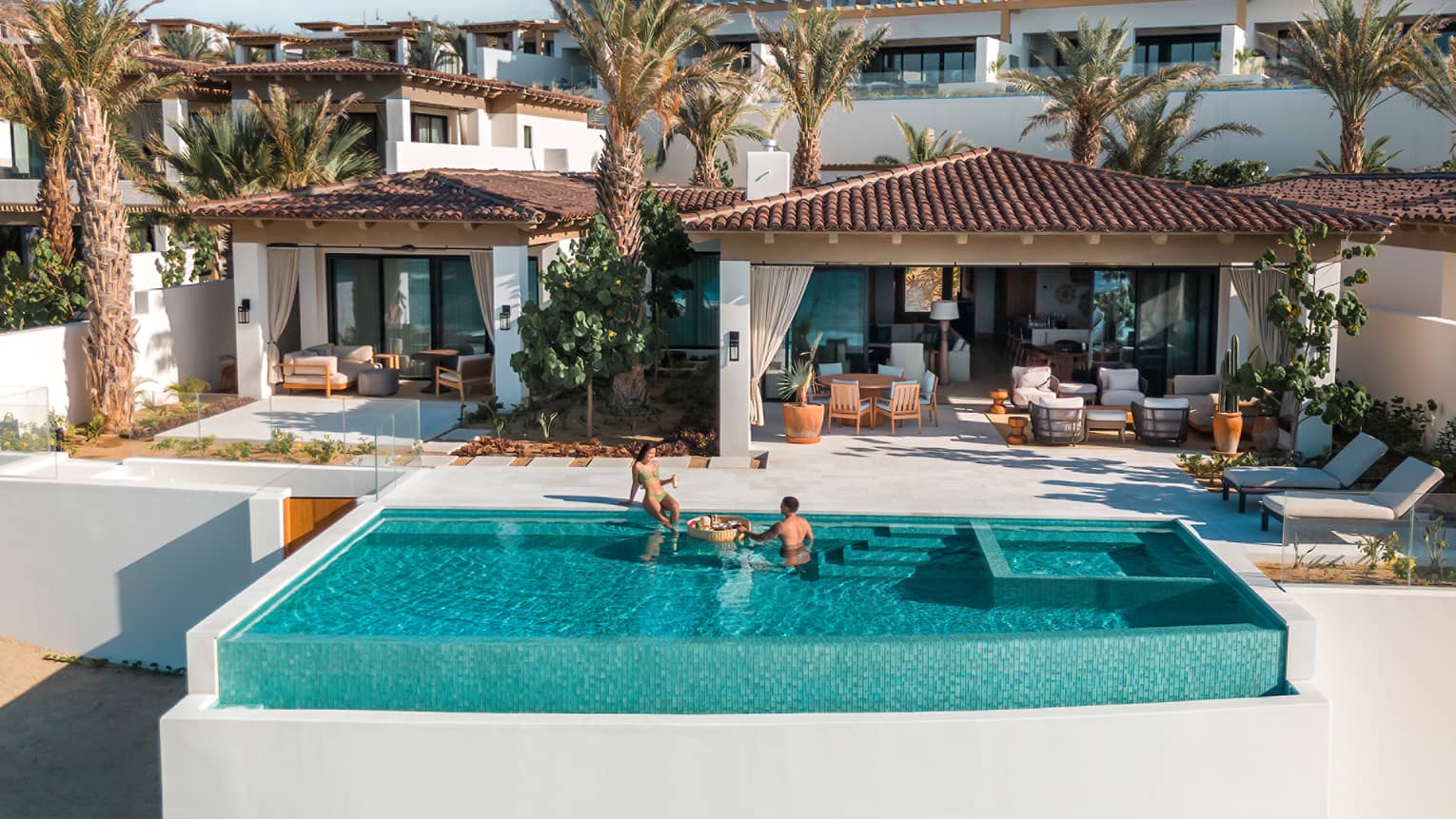 Two people relax in infinity pool at tropical resort