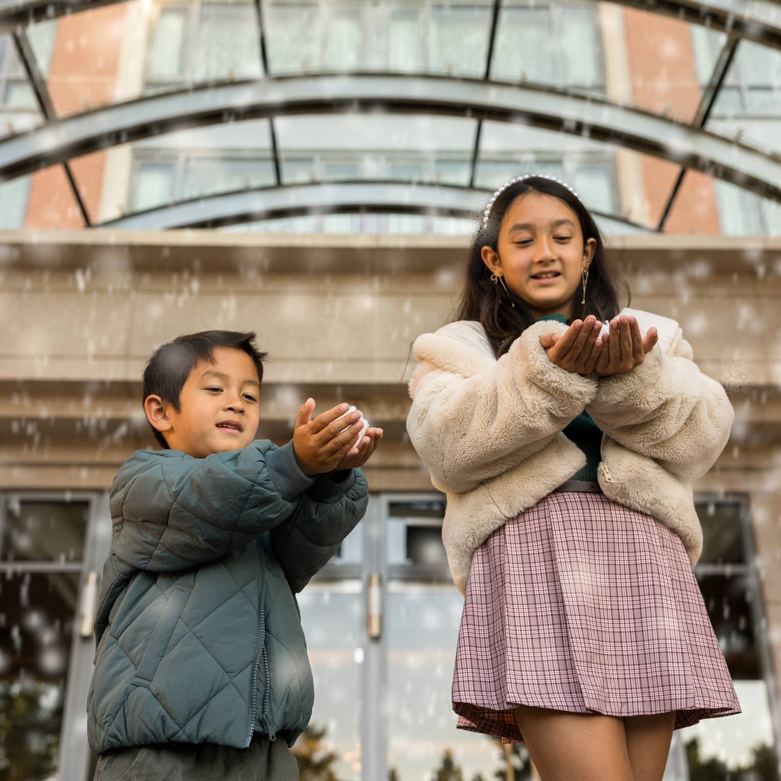 Two kids play with faux snow falling from the ceiling of a hotel entrance