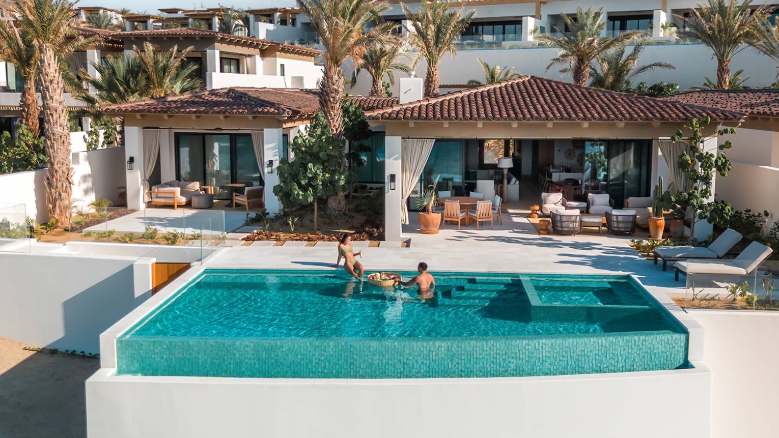 Two people relax in infinity pool at tropical resort