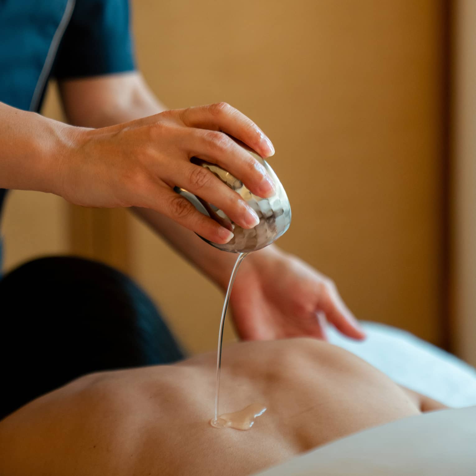 Spa therapist hand pouring oil on person's back