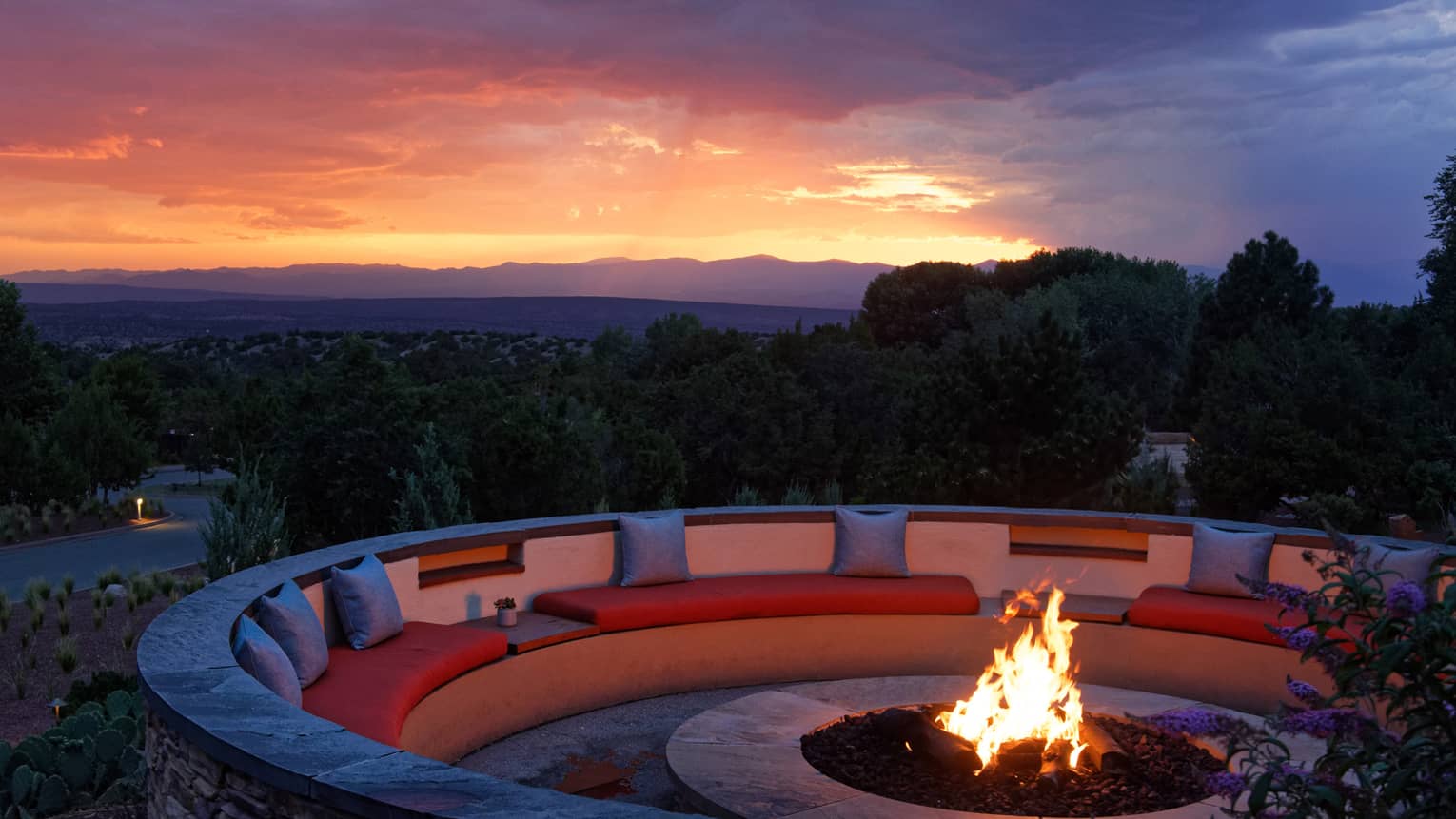 Fire pit with seating surrounding it and a sunset in the background.