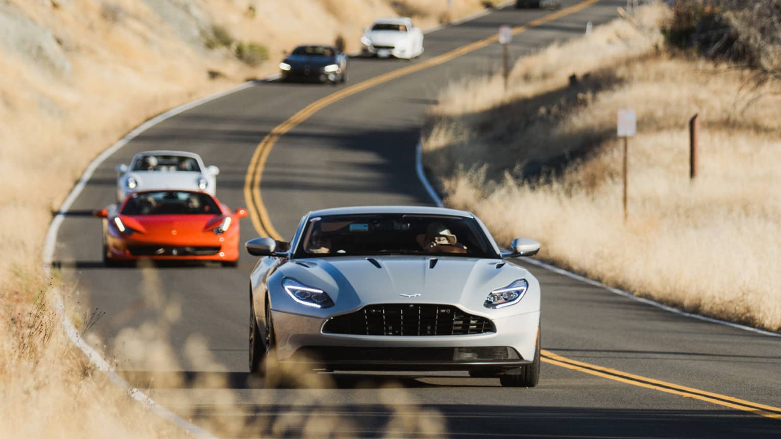 Multiple cars driving on a curved road surrounded by trees and bushes.