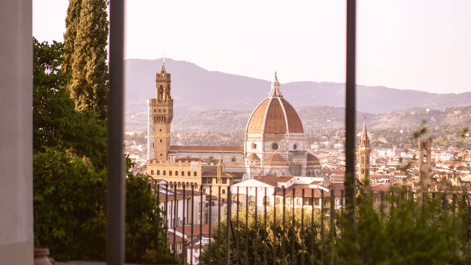 Distant view of the Florence Cathedral and the surrounding city, seen from a large, high-up fenced patio with potted plants.