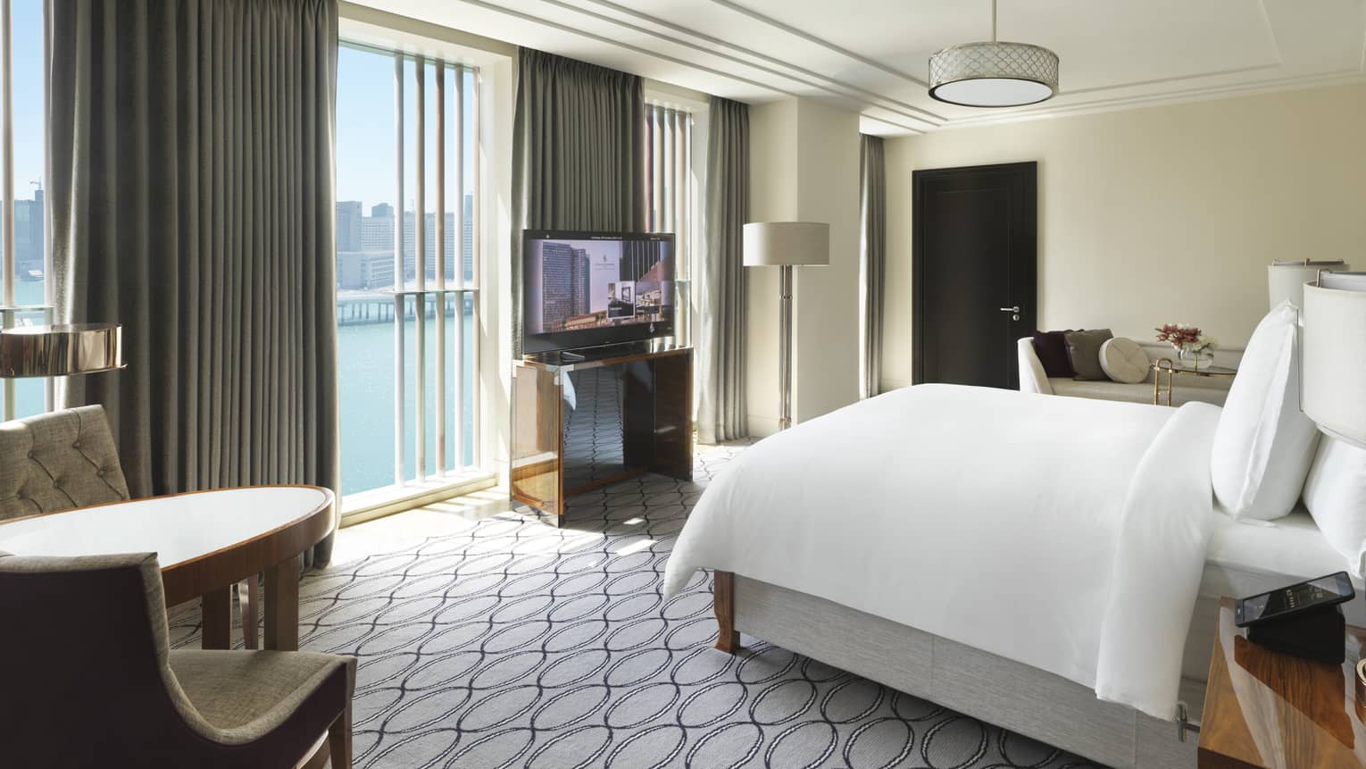 Hotel room with king bed, table with two chairs, TV and wall of windows